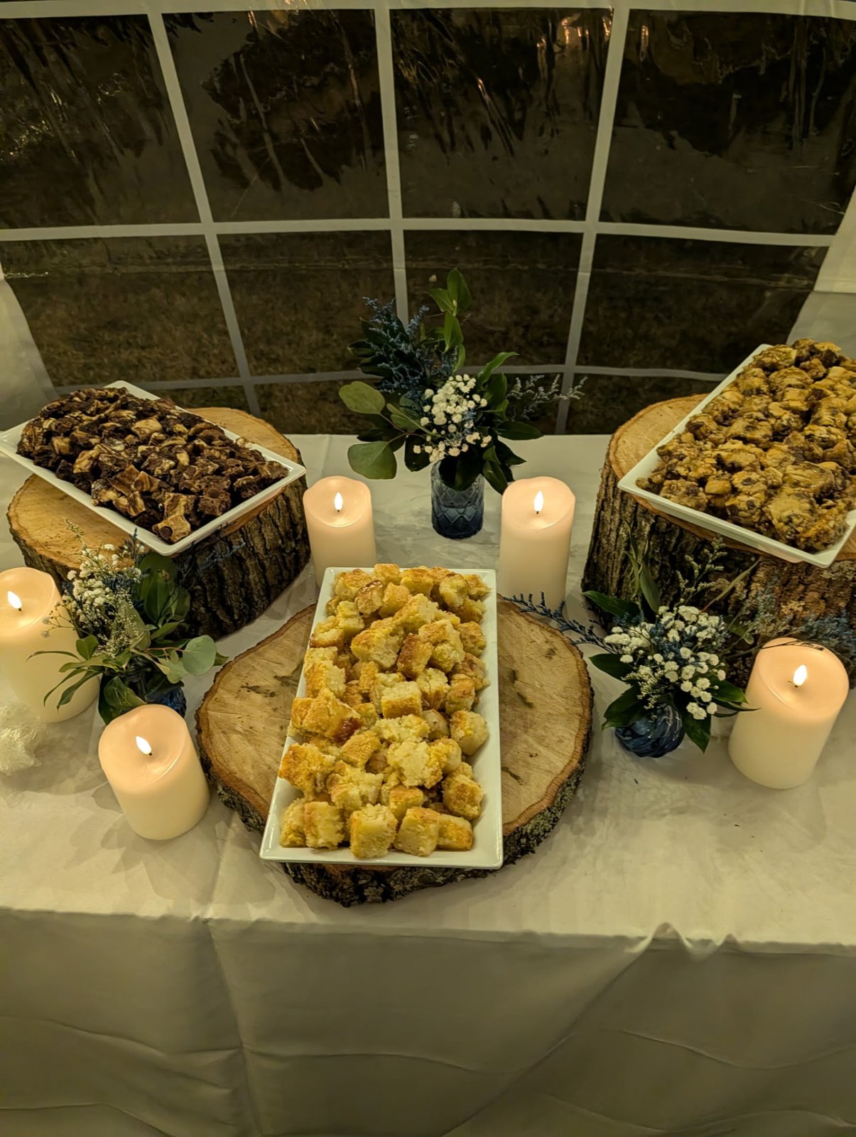 Rustic dessert table with cobbler and sweets on wood rounds surrounded by candles and greenery